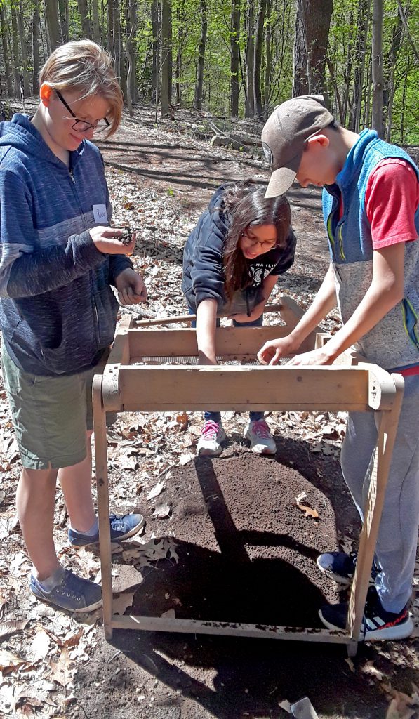 This is an image of three students using a screening tool to sift through dirt