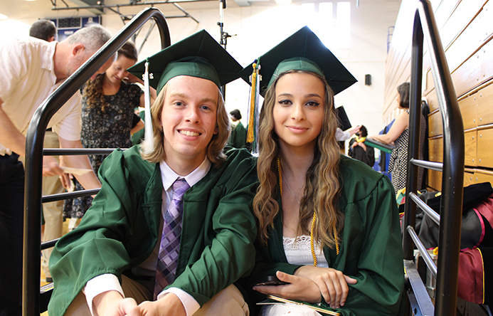 Two students in caps and gowns sitting together at graduation.