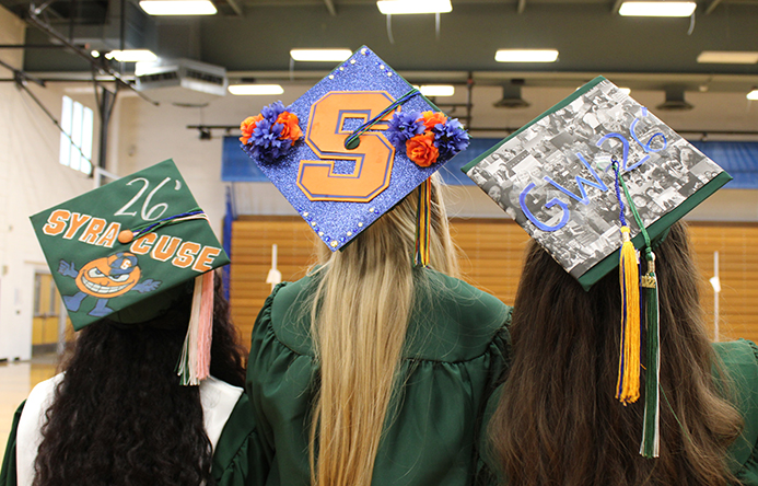 Three students with backs facing toward the camera, showing off graduation caps.