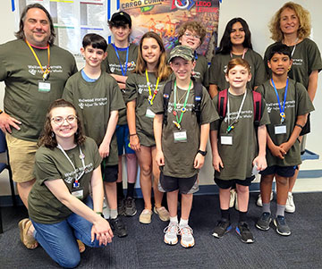 Several students and three educators from the robotics team smiling at competition.