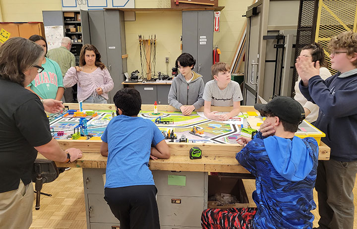 Students stand around a table to program a robot together.