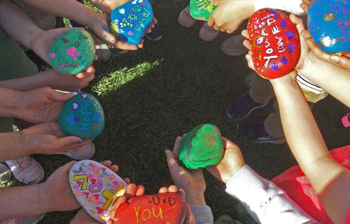 Students holding out painted rocks in a circle.