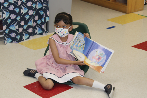 Child showing camera a book in a classroom.