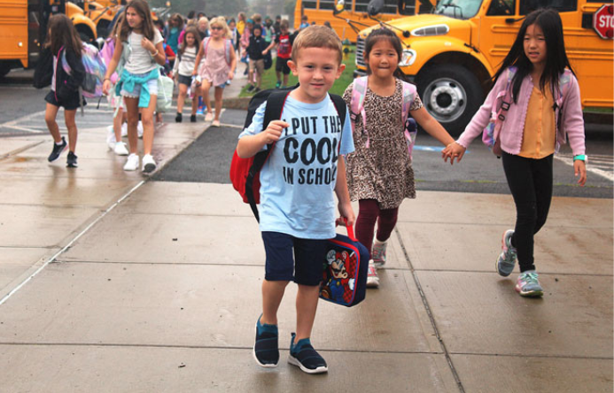 A younger child wearing a backpack pauses for the camera as he walks into school