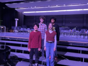 Four students standing on music risers smiling at the camera