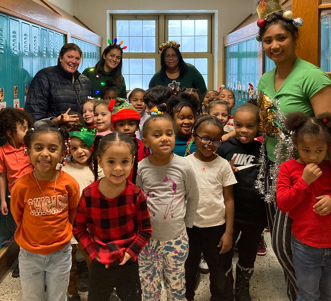 Dozens of young children are in a hallway standing next to one another and smiling for the photo