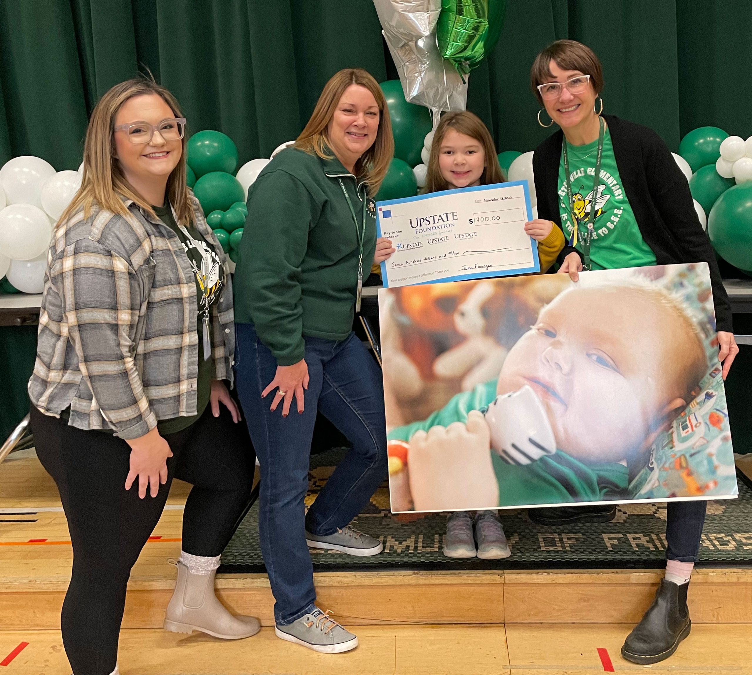 First-grade student June stands with her teacher and other school staff members while holding a photo of her brother