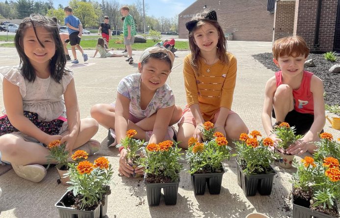 Children potting flowers outside of school on a sunny day