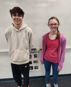 Hudson Brown and Elizabeth Hansen standing in front of a whiteboard smiling and posing for the camera.