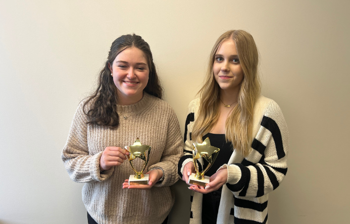 two female students each holding a gold trophy in front of a white wall