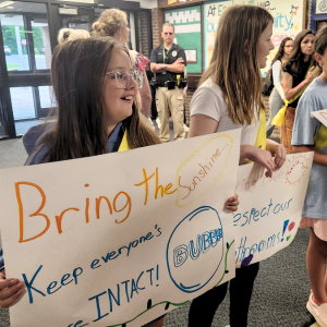 a group of students standing shoulder-to-shoulder holder posters and smiling