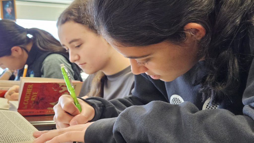 students working in classroom, an up close image of student writing notes while looking at a book