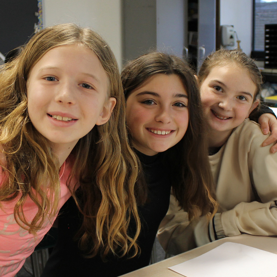 Three middle school students positioned together smiling.