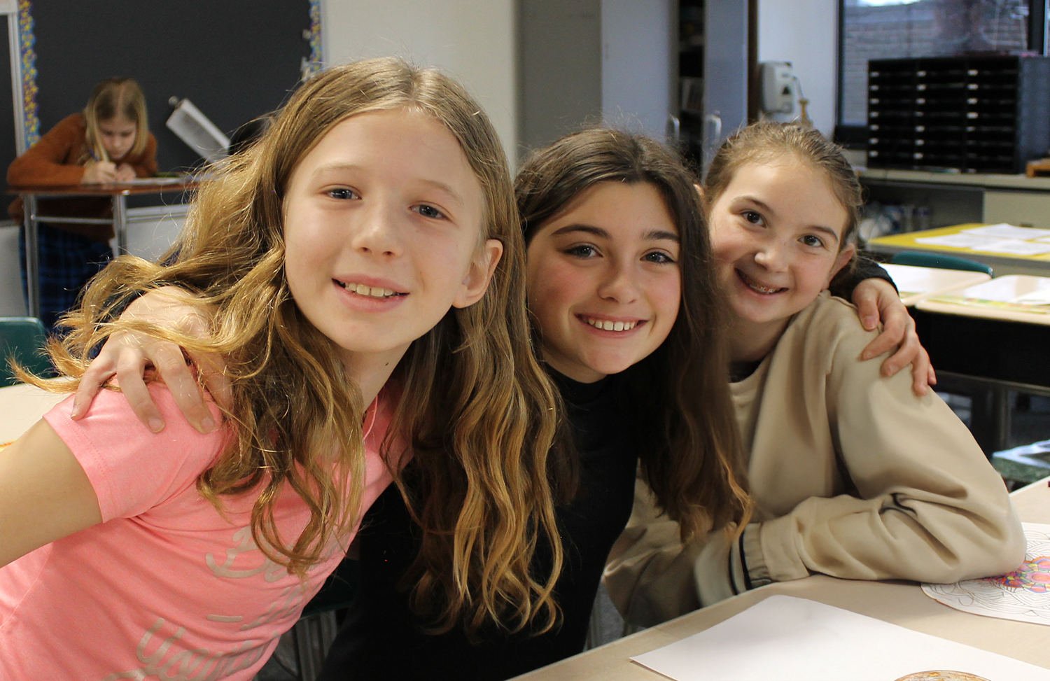 Three middle school students gather closely smiling.