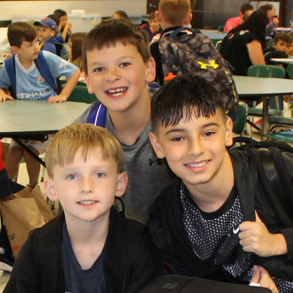 Three middle school students smiling together in the cafeteria.
