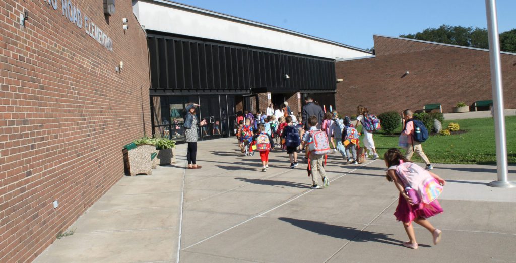 young students running to the front of school building to go inside for first day