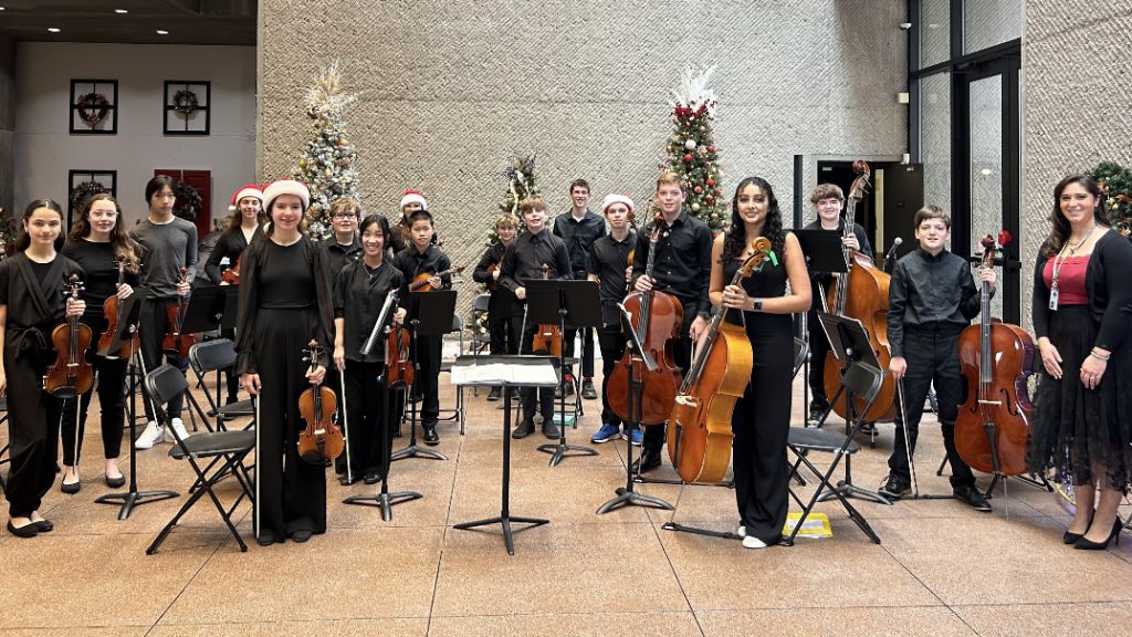 student orchestra standing together holding instruments