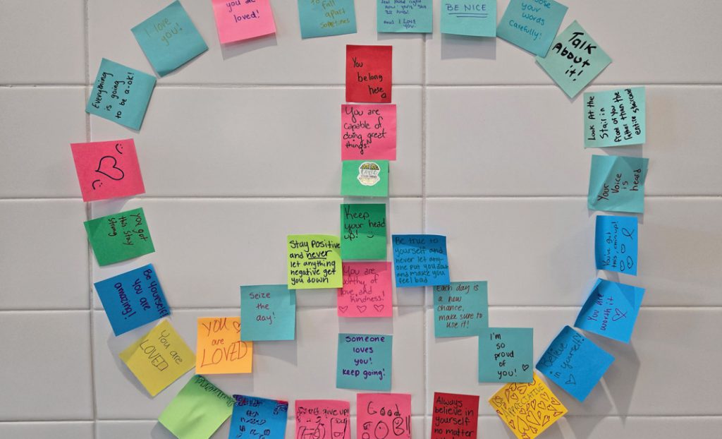 Post it notes displaying positive messages such as "you are loved" and "talk about it" in the shape of a peace symbol