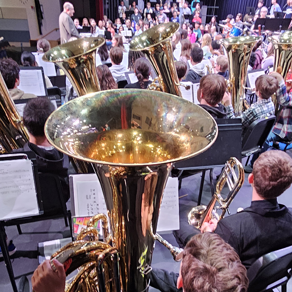 Several students holding tuba await their turn during an orchestra performance.