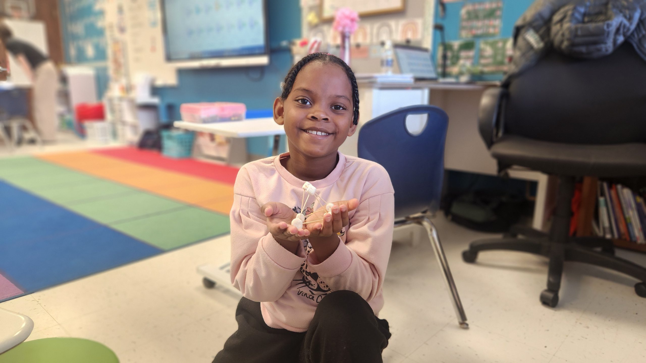 An elementary school student holds a structure of marshmallows and wooden rods.