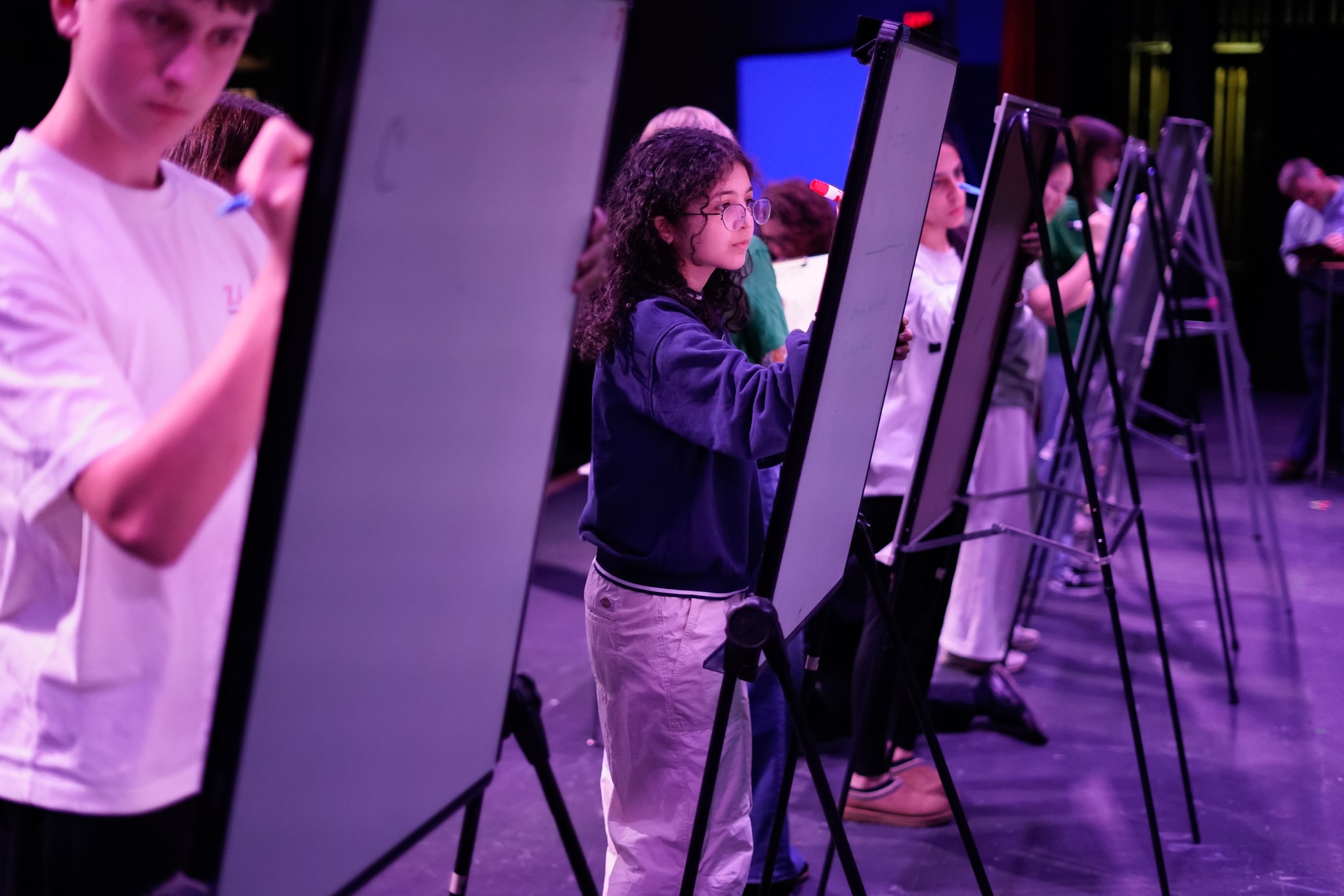 Student work intensely at easels on a stage.
