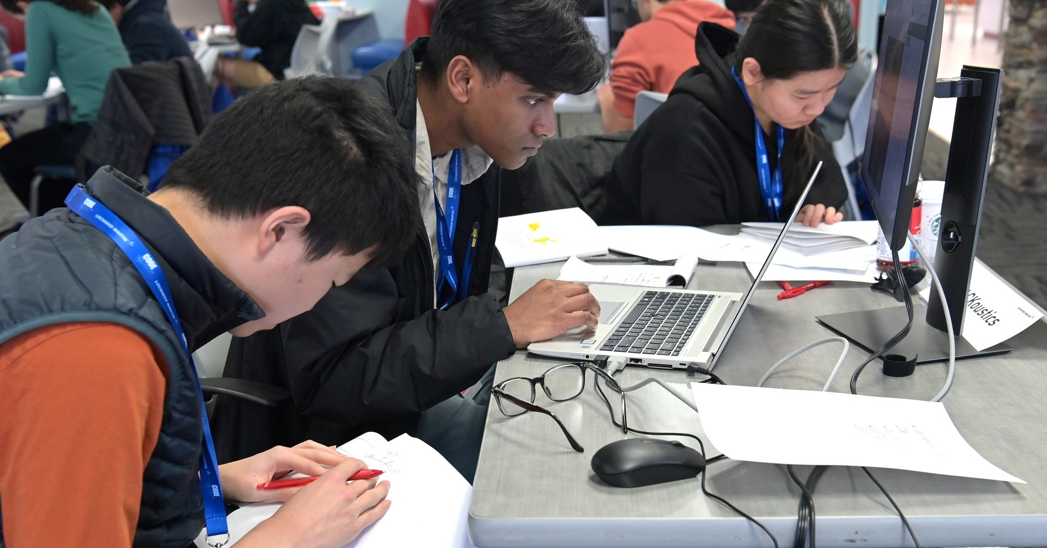 One high school student peers intently on to a laptop while two others work with worksheets.