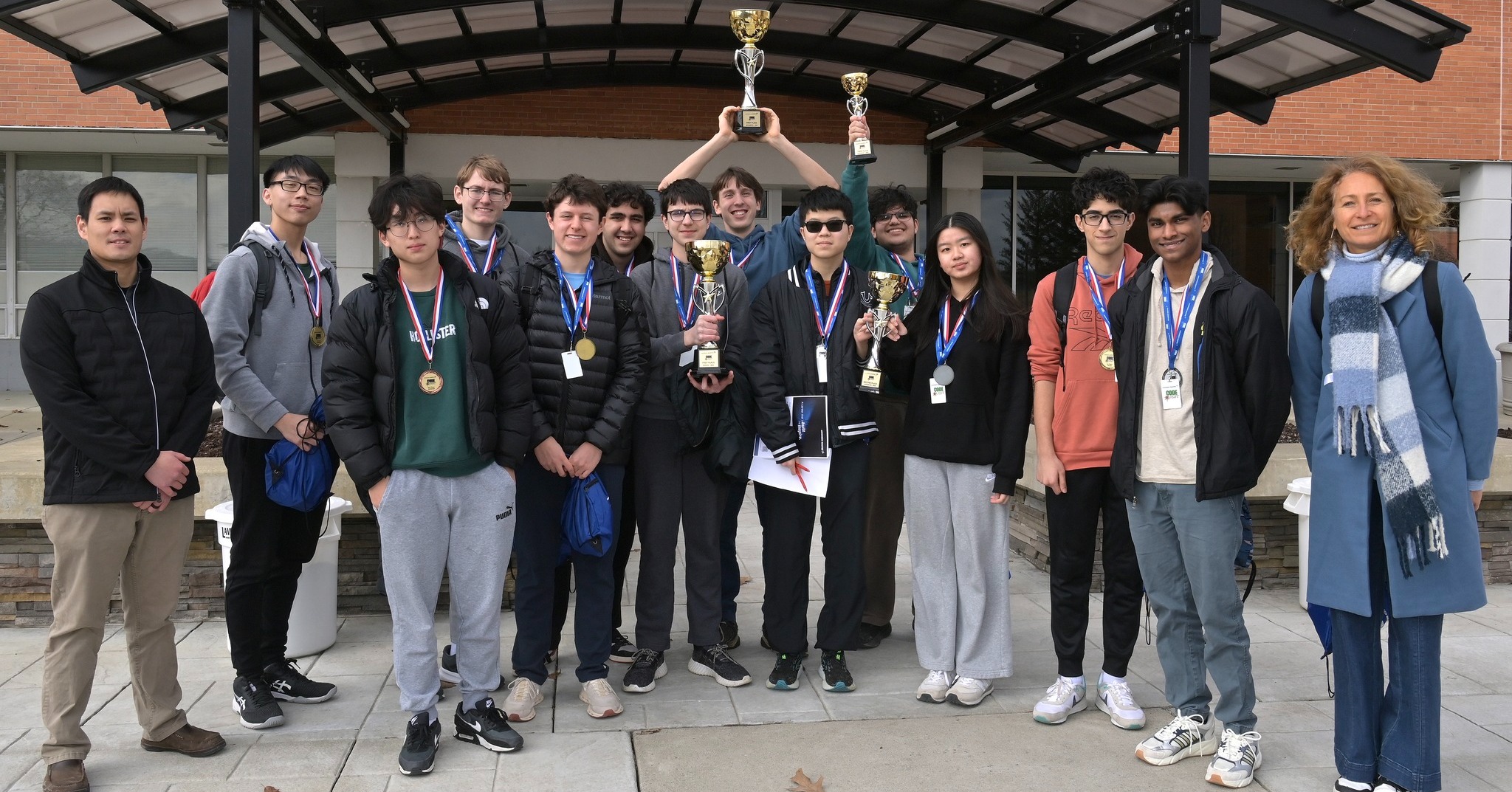 Several students display medals and three trophies.