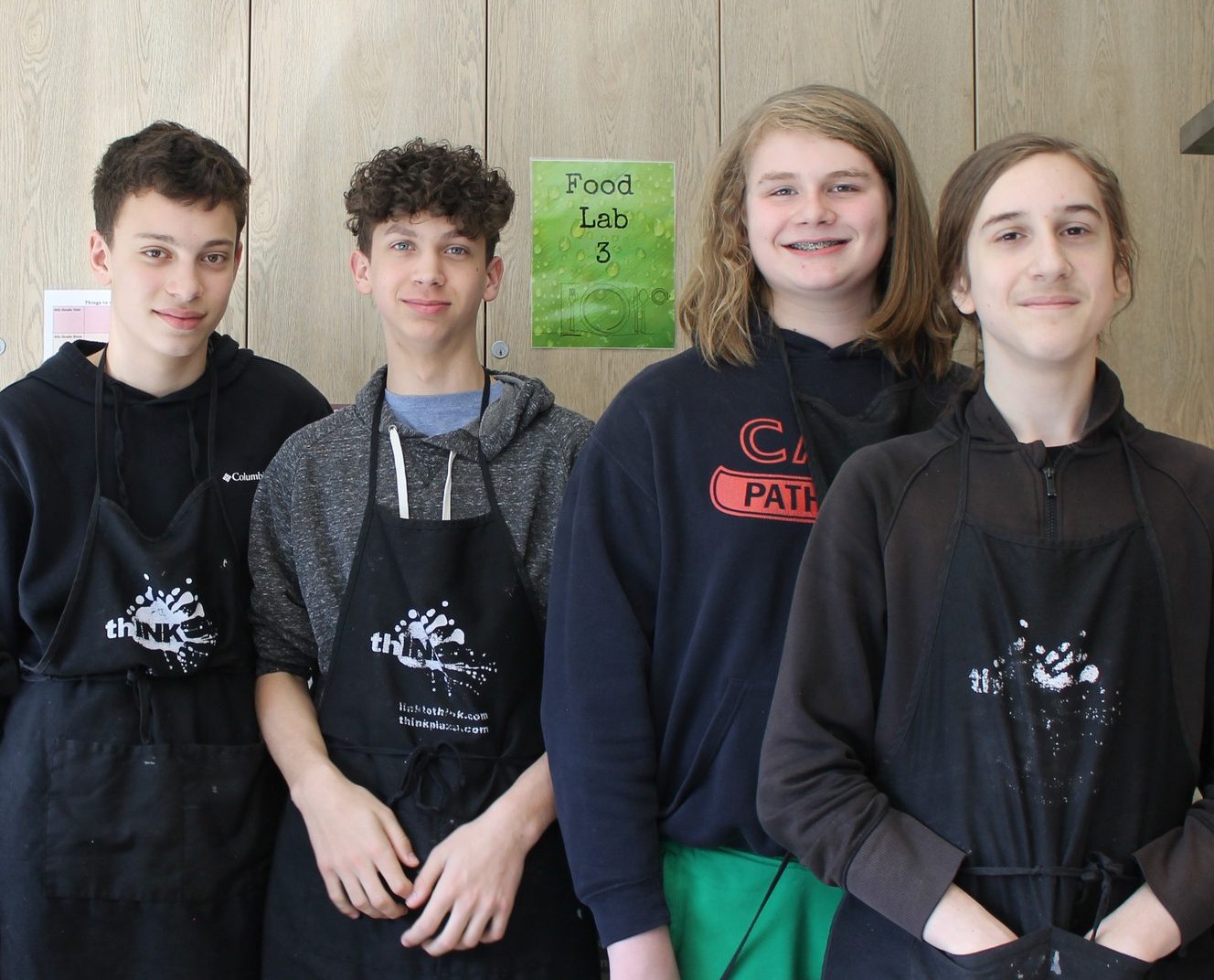 Five middle schoolers stand together with black aprons.