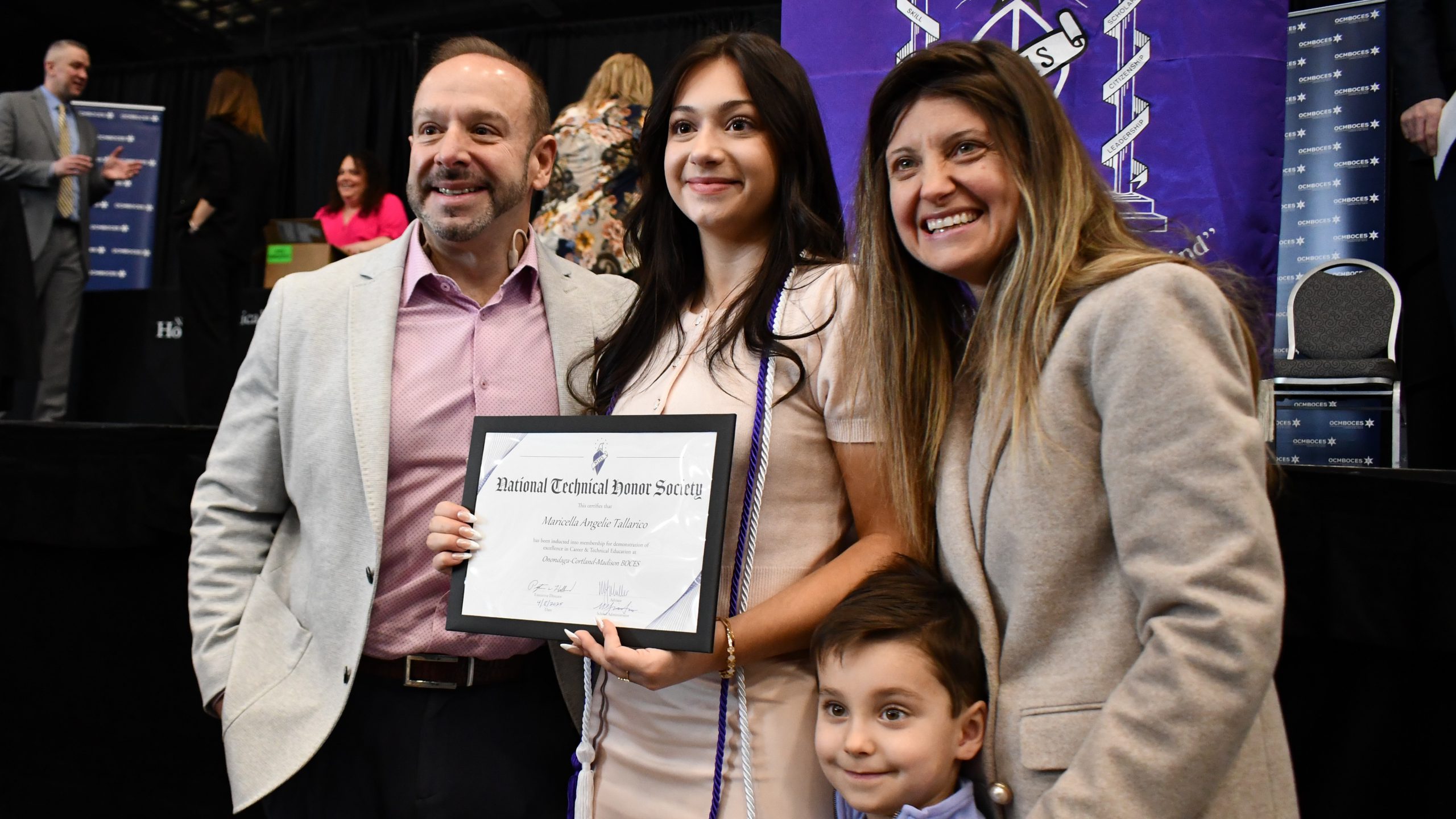 Maricella Tallarico holding her honor society certificate and standing with her family, posing for a picture