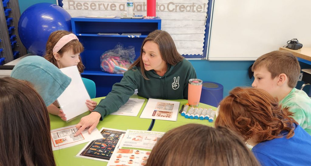 A teacher explains a worksheet at a table filled with students.
