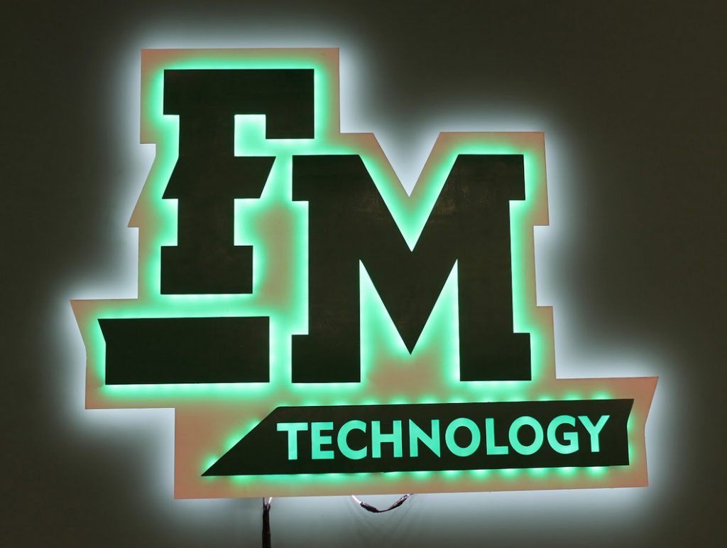 A glow-in-the-dark sign that says "FM Technology" hanging on a wall.