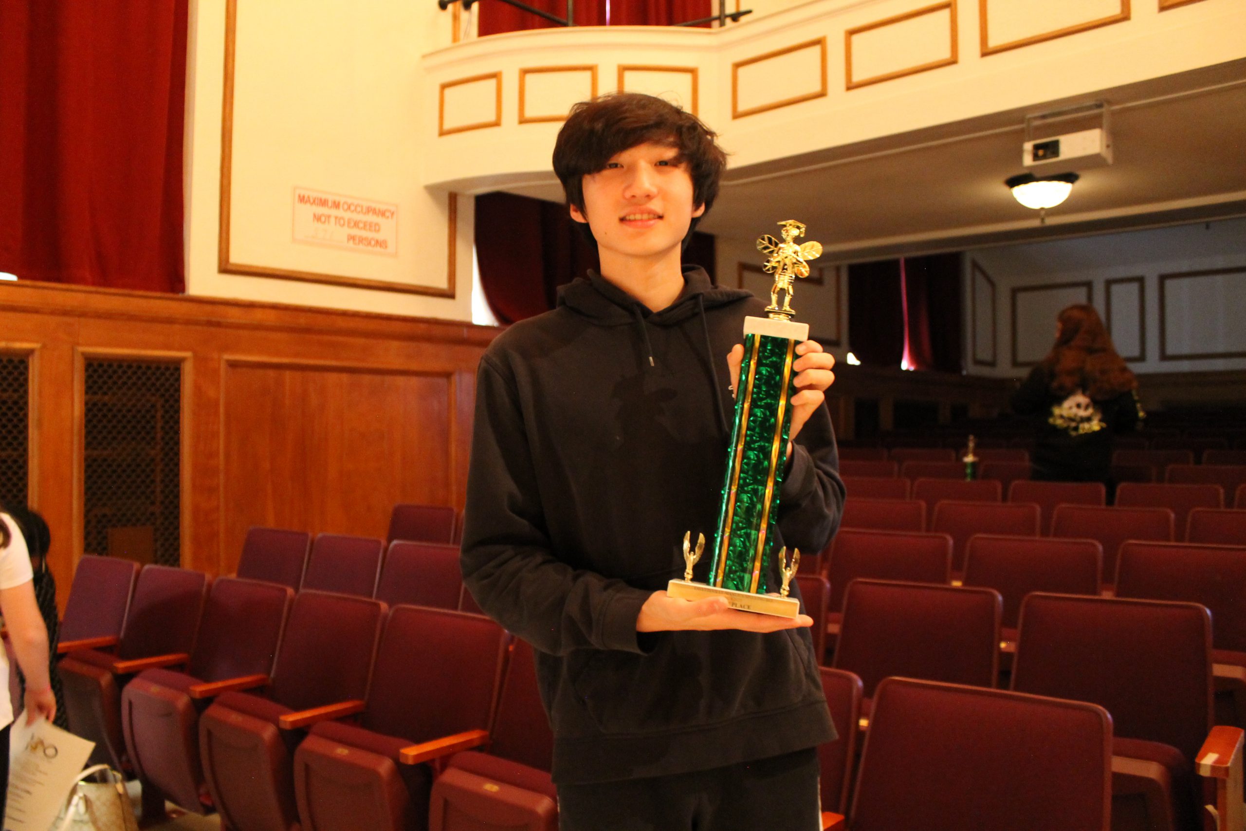 A student holds a large trophy in an auditorium.