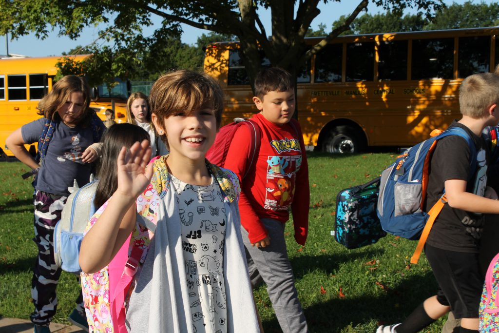 young student walking from bus waving at camera smiling