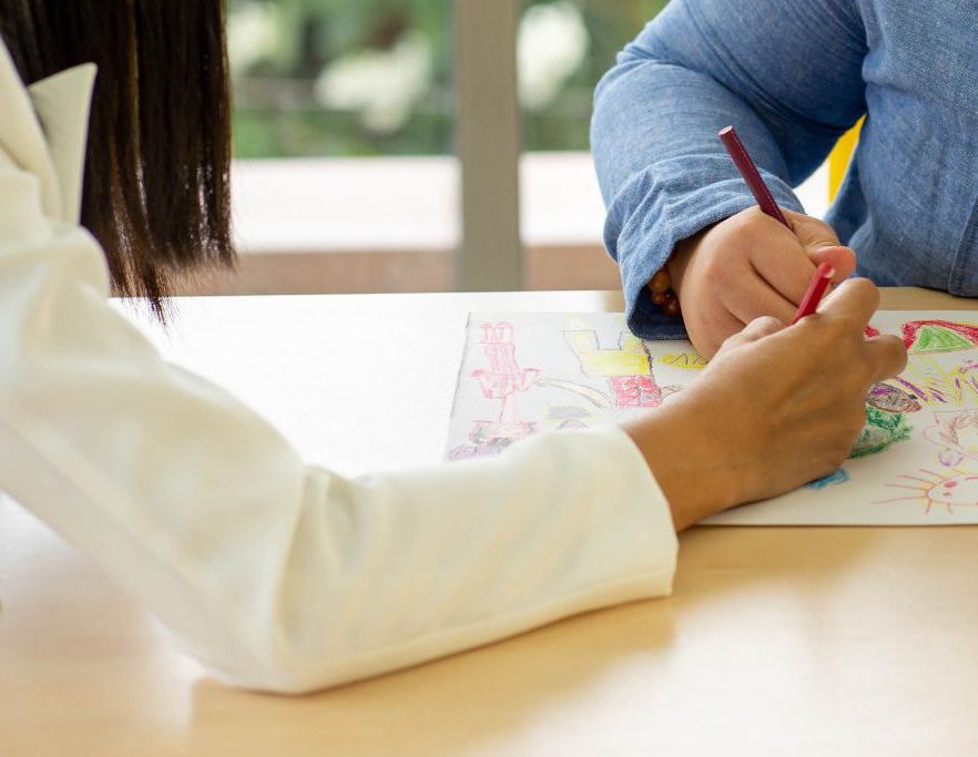The hand of an adult coloring a picture with the hand of a student.