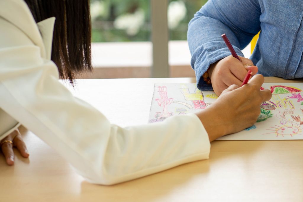 The hand of an adult coloring a picture with the hand of a student.