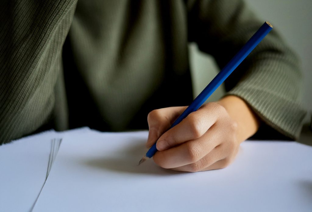 A closeup of a child's hand positioned to write on a black sheet of paper.