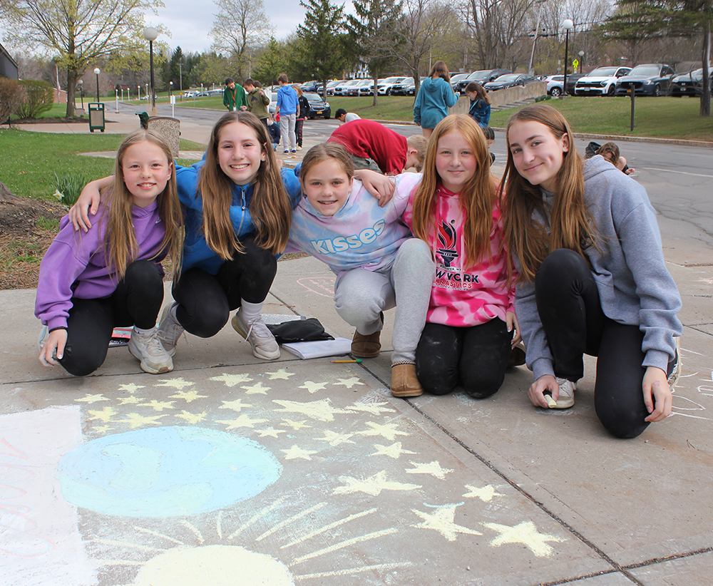 A group of students crouch near their sidewalk chalk art.