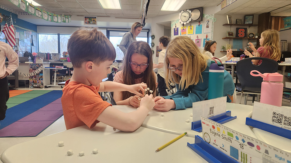 Three students work closely together on building a 3D structure.