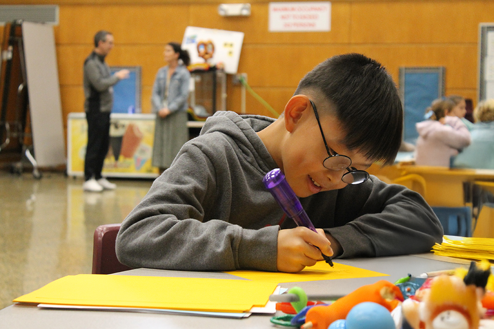 A student with glasses works intently with a giant pen.