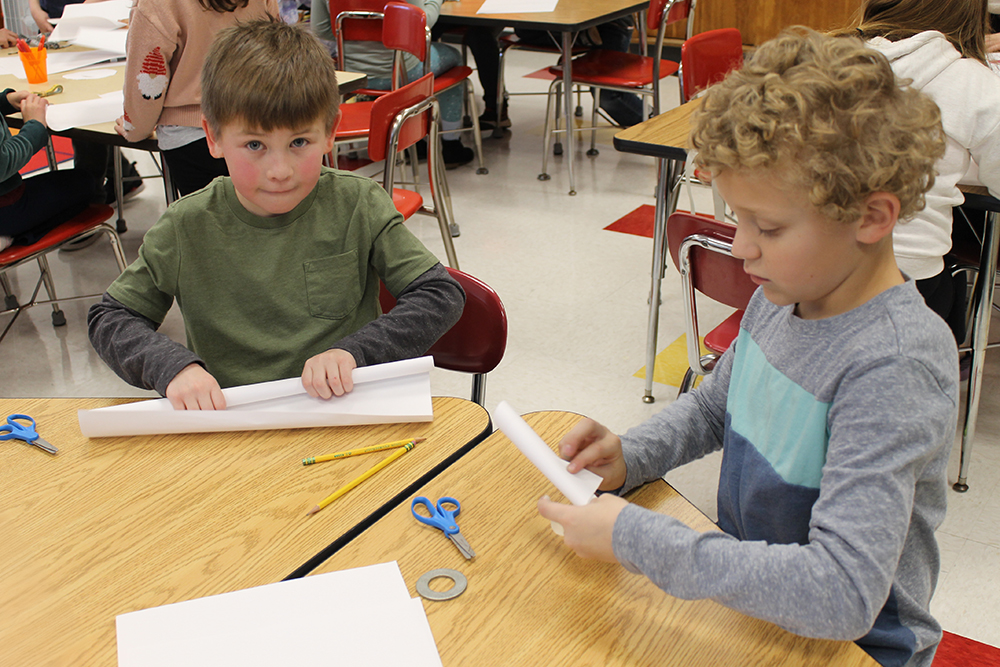 Two elementary students roll large sheets of paper for a construction project.