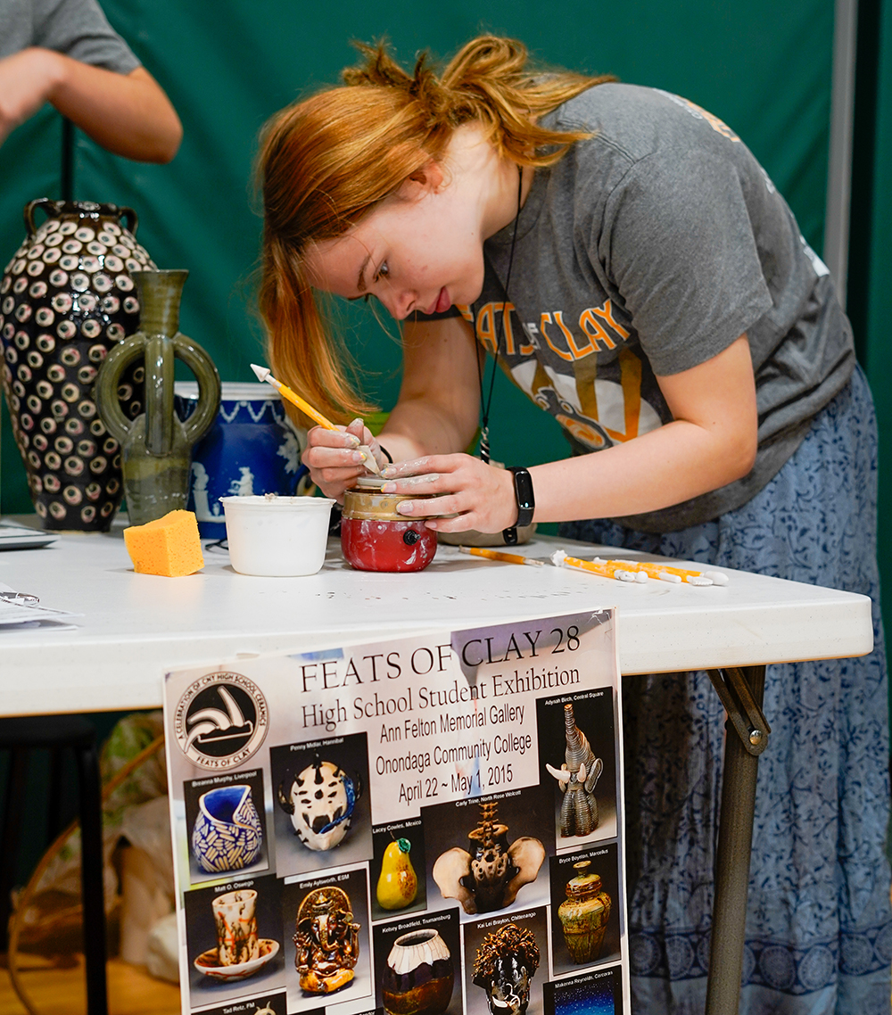 A student bends over for closeup work on a pottery piece.