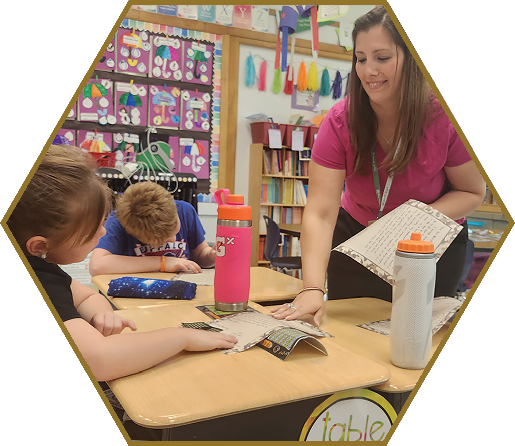 A teacher leans over tables with two students working.