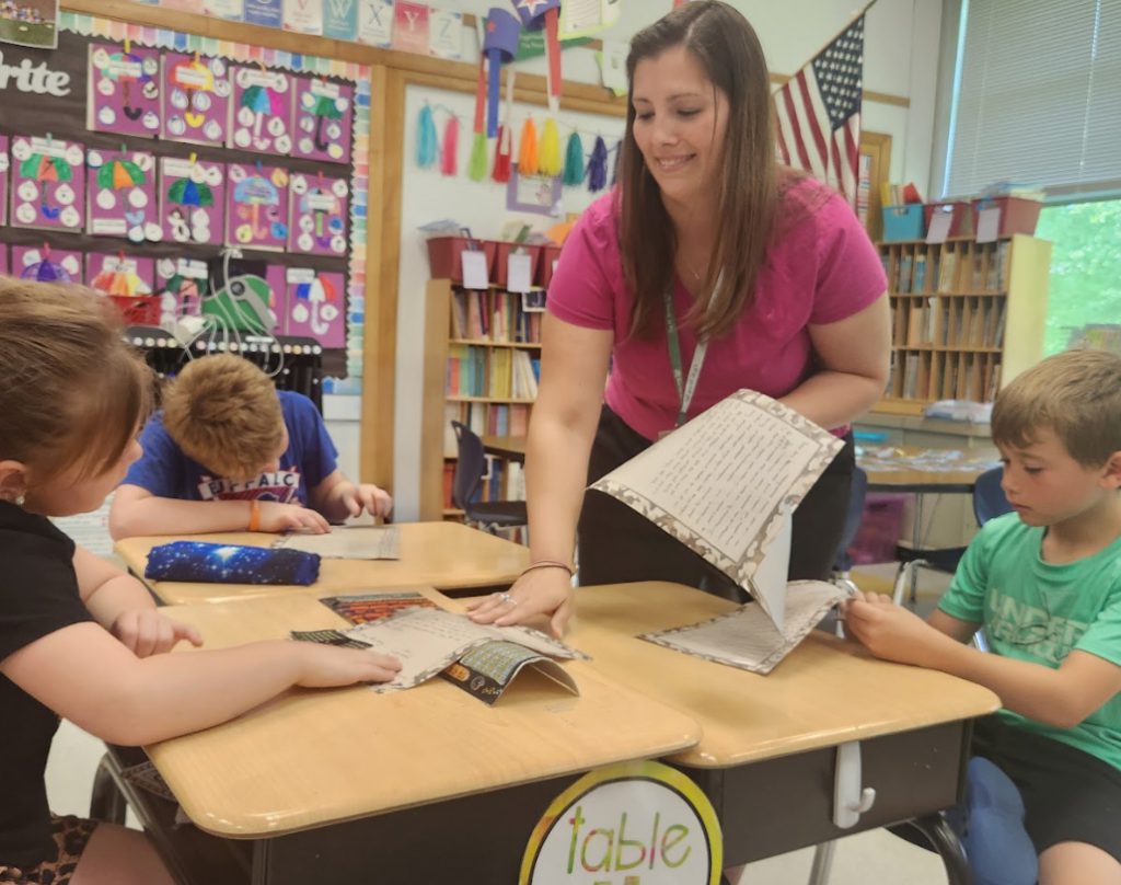 A teacher leans over students and hands them worksheets.