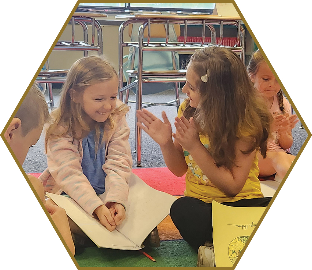 One first grade student encourages another to sing and clap.