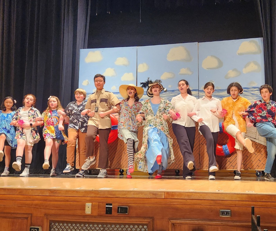 Middle School students lock arms and kick their left leg on a stage.