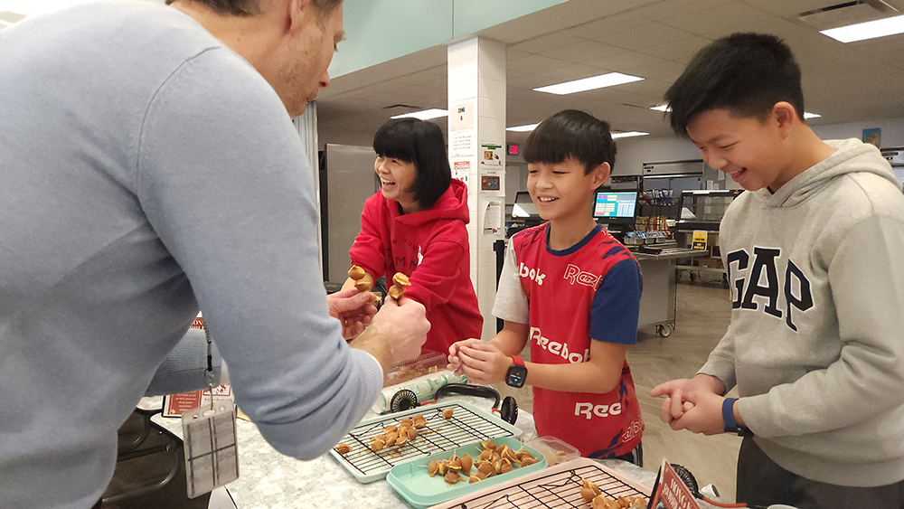 Two students and an adult serve toothpick snacks to a staff member.