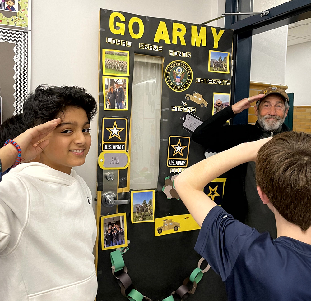 Two students and one adult salute around a "Go Army" display.