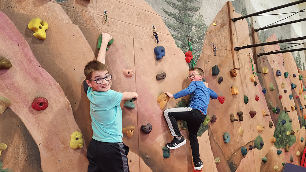 Two elementary aged child perch happily on a climbing wall.
