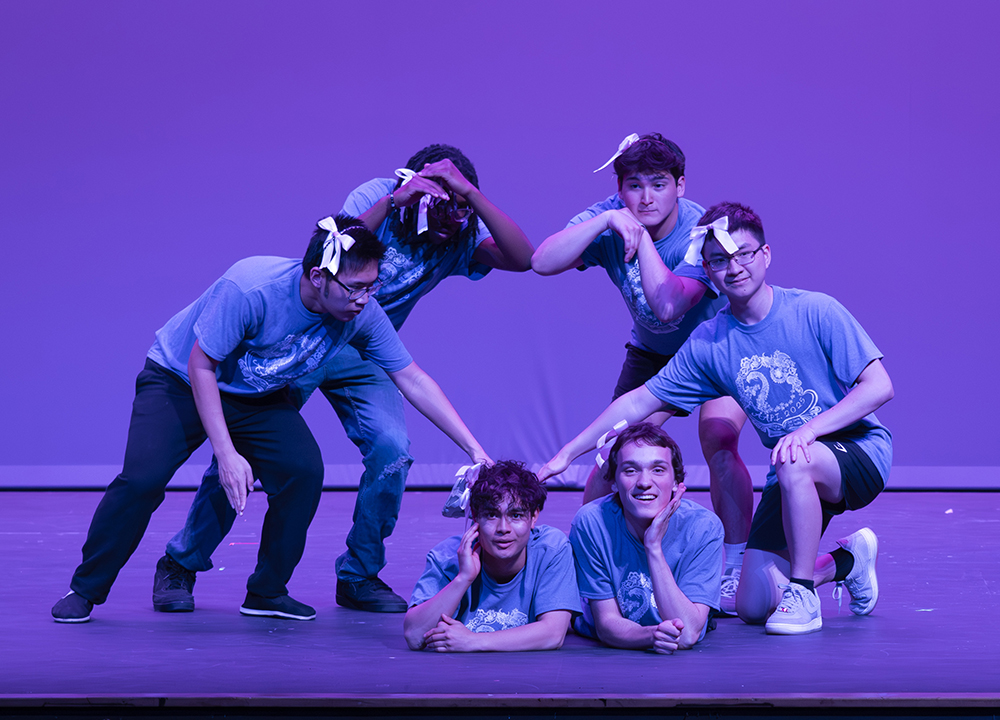 Several high school students form the shape of a heart on a stage.