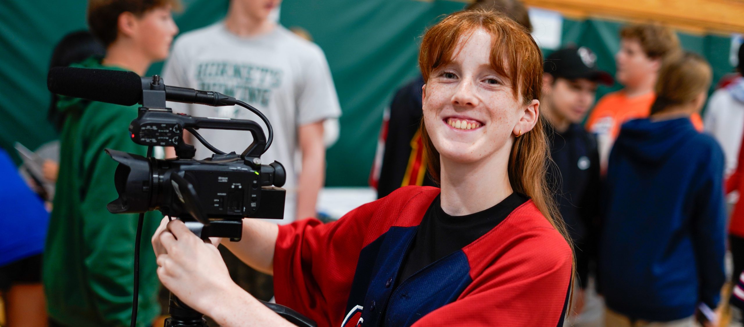 A high school AV student proudly smiles from behind the camera.